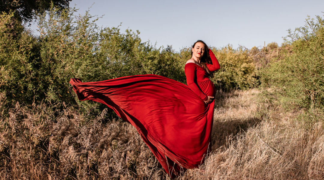 Pregnant woman wearing flowing red dress against a desert landscape.
