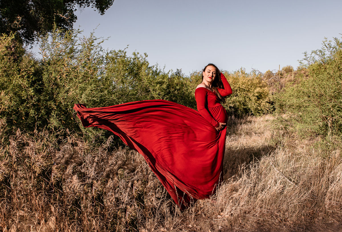 Pregnant woman wearing flowing red dress against a desert landscape.