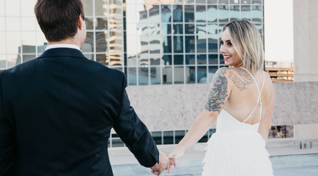 Couple in wedding outfits looking at each other with a downtown background.